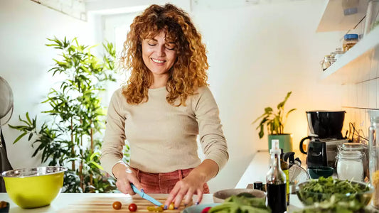 A smiling woman with curly hair happily chops fresh vegetables in a bright, modern kitchen, embodying healthy sugar-free eating and a positive post-vacation reset.