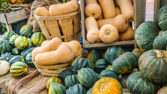 Colorful winter squash varieties, including butternut, acorn, and kabocha, at a farmer's market.