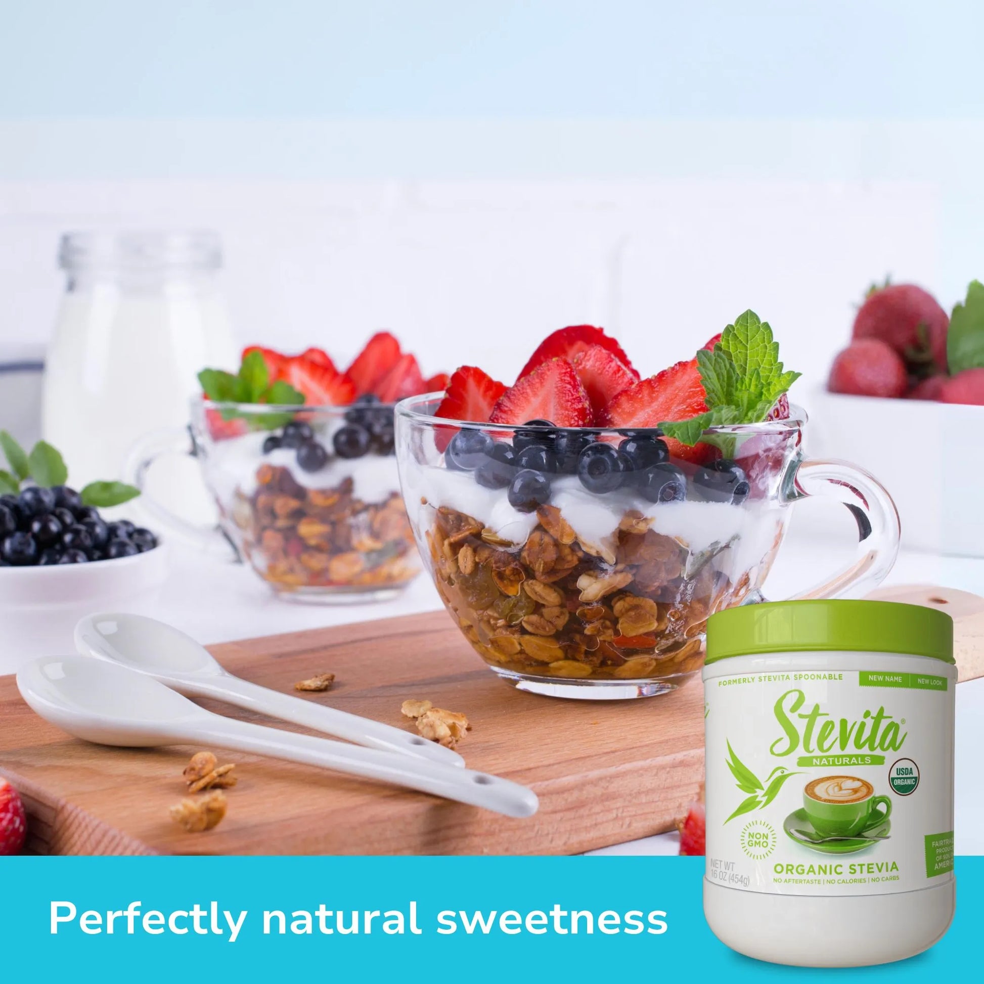 Two glass cups filled with yogurt, granola, strawberries, and blueberries on a table. A Stevita Organic Stevia jar is in the foreground. Text reads "Perfectly natural sweetness."