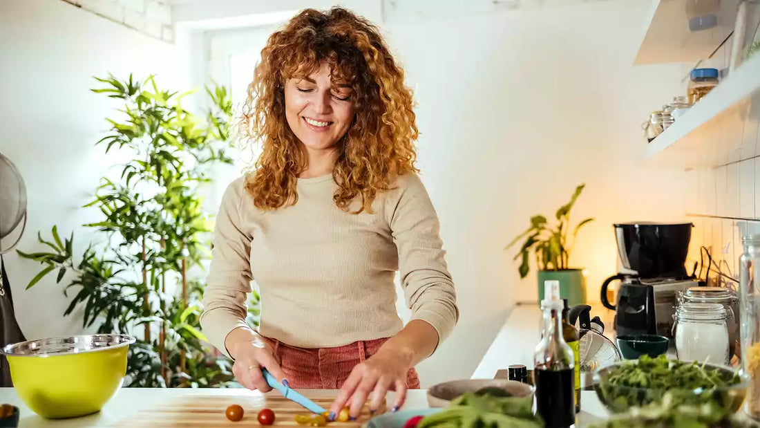  A smiling woman with curly hair happily chops fresh vegetables in a bright, modern kitchen, embodying healthy sugar-free eating and a positive post-vacation reset.