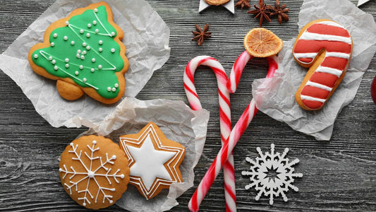 Overhead view of various Christmas-themed sugar-free cookies made with stevia—a green Christmas tree, a snowflake, and a star—along with two striped candy canes, all resting on a dark wooden background.