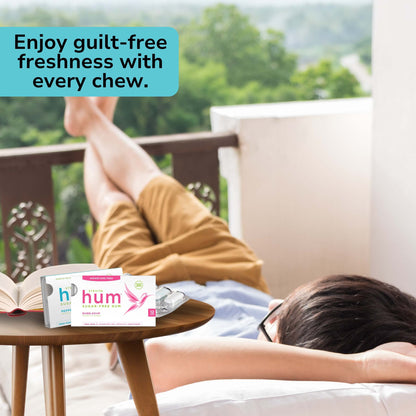 A person relaxes on a balcony with lush greenery in the background, legs up, conveying tranquility. Foreground features sugar-free hum gum and a book on a table. Text reads: "Enjoy guilt-free freshness with every chew."