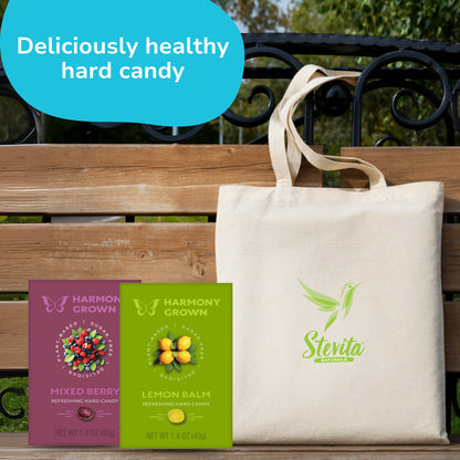 Tote bag with Stevita Naturals logo on a wooden bench, displaying two packets of Harmony Grown hard candy, Mixed Berry and Lemon Balm. Text reads "Deliciously healthy hard candy."